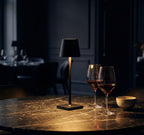 Black table lamp on a marble surface with two wine glasses and a bowl in a dimly lit room.